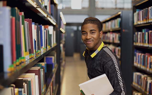 student standing in the library looking to get his online library and information science degree
