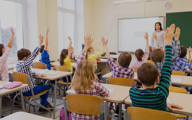 teacher in front of a class room of eager children raising their hands